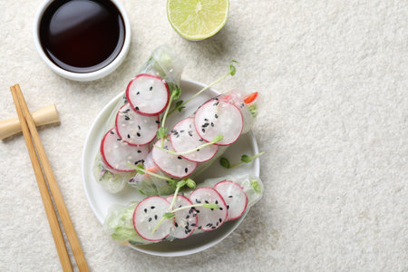 Delicious spring rolls, chopsticks, soy sauce and lime on light gray table, flat lay. Space for text