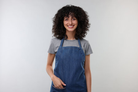 Happy woman wearing kitchen apron on light grey background. Mockup for design