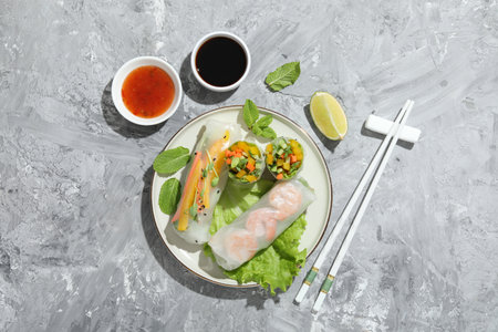 Tasty spring rolls served on gray textured table, flat lay. Space for text
