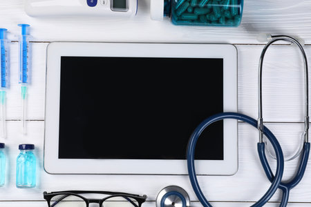 Flat lay composition with modern tablet and medical supplies on white wooden table