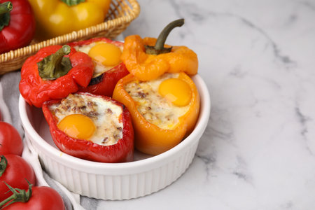 Delicious stuffed peppers with eggs in bowl on white marble table. Space for textの写真素材