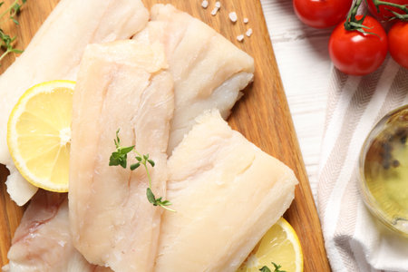 Pieces of raw cod fish, lemon and tomatoes on white wooden table, top view