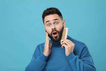 Surprised young man combing beard on light blue backgroundの写真素材
