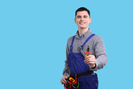 Young man holding pliers on light blue background, space for text
