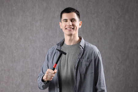 Young man holding hammer on grey backgroundの写真素材