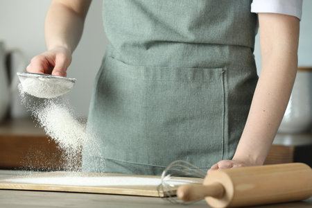 Woman sieving flour at table in kitchen, closeupの写真素材