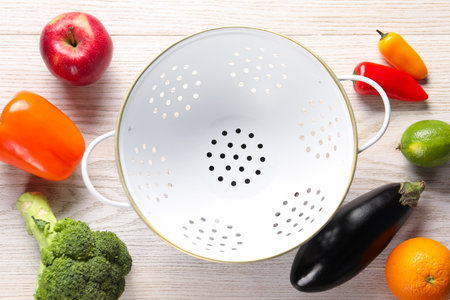 Empty colander, fresh fruits and vegetables on white wooden table, flat layの写真素材
