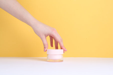 Woman with jar of cream on yellow background, closeupの写真素材