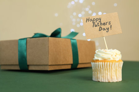 Happy Father's Day. Tasty cupcake with greetings and gift box on green table, closeupの写真素材