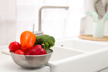 Fresh clean vegetables in colander on countertop near sink. Space for text