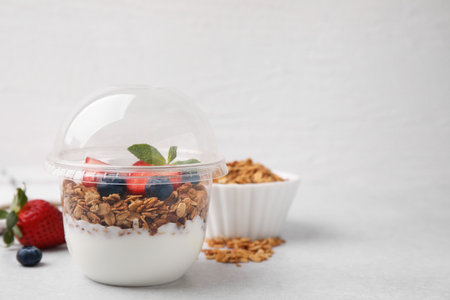 Tasty granola with berries and yogurt in plastic cup on light table, space for textの写真素材