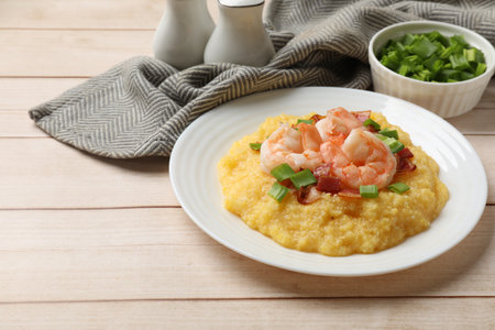 Plate with fresh tasty shrimps, bacon, grits and green onion on light wooden table, space for textの写真素材