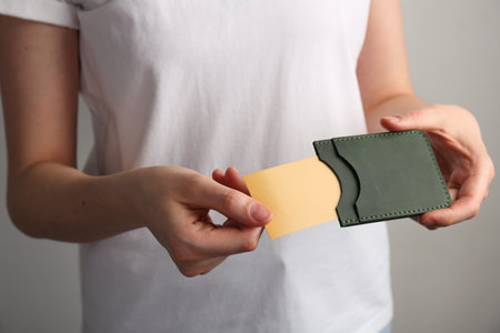Woman holding leather business card holder with card on gray background, closeup