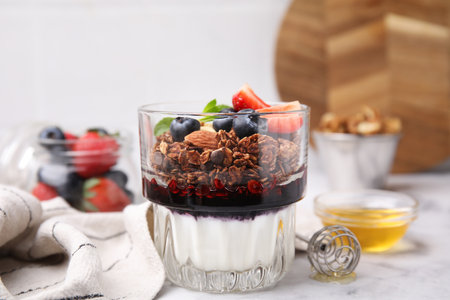 Tasty granola with berries, jam and yogurt in glass on white tableの写真素材
