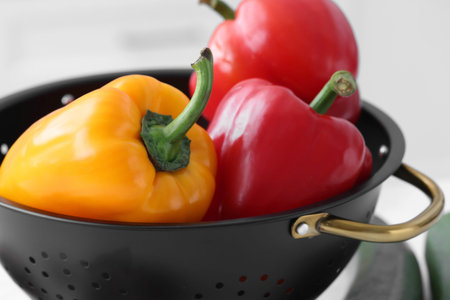 Fresh bell peppers in black colander on blurred background, closeupの写真素材