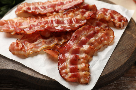 Board with fried bacon slices on wooden table, closeup
