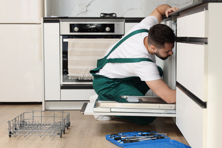 Serviceman repairing dishwasher near toolbox in kitchenの写真素材