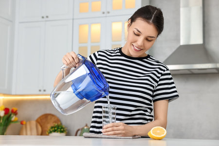 Woman pouring water from filter jug into glass in kitchenの写真素材