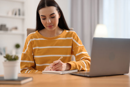 Young woman writing down notes during webinar at table in roomの写真素材