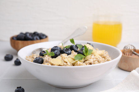 Tasty oatmeal with blueberries, mint and almond petals in bowl on white tiled tableの写真素材