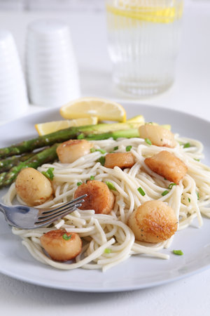 Delicious scallop pasta with asparagus, green onion and lemon served on white table, closeupの写真素材