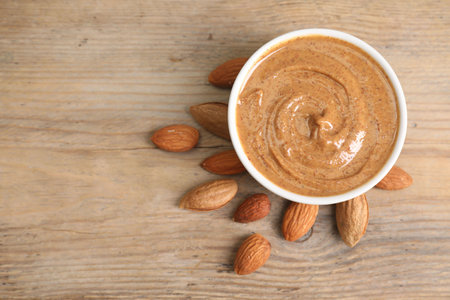 Delicious nut butter in bowl and almonds on wooden table, top view. Space for textの写真素材