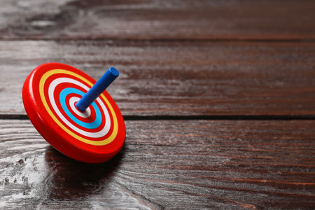 One bright spinning top on wooden table, closeup. Space for text