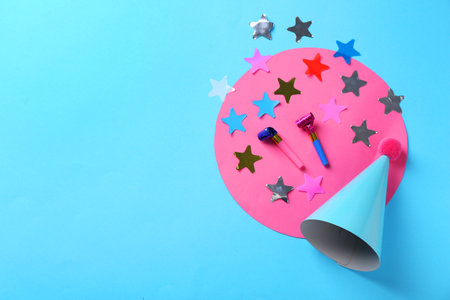Party hat, confetti and blowers on light blue background, flat lay. Space for textの写真素材