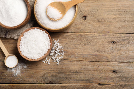 Natural salt in different dishware on wooden table, flat lay. Space for textの写真素材