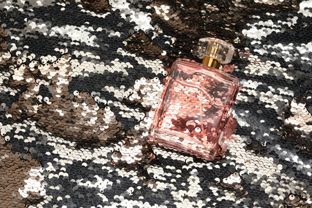 Luxury perfume in bottle on fabric with silver sequins, top view