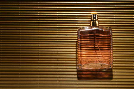 Luxury women's perfume. Sunlit glass bottle on golden surface, top view. Space for textの写真素材