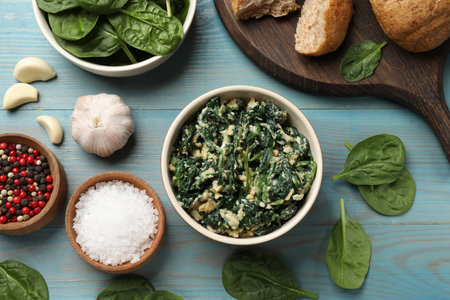 Tasty spinach dip with egg in bowl, bread and spices on light blue wooden table, flat layの写真素材