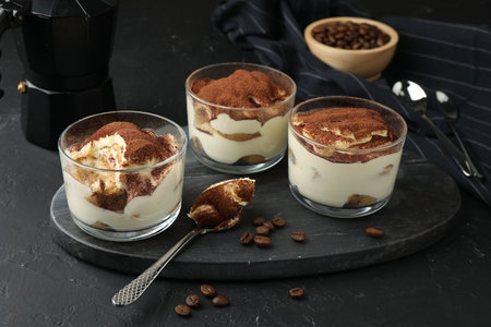 Delicious tiramisu in glasses, spoon and coffee beans on black tableの写真素材
