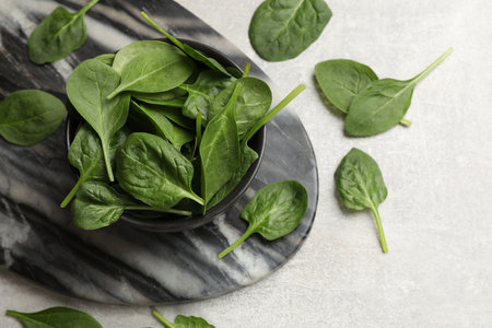 Fresh spinach leaves in bowl on light textured table, flat layの写真素材