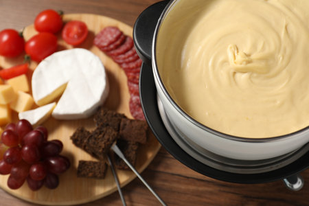 Fondue with tasty melted cheese, forks and different snacks on wooden table, above viewの写真素材
