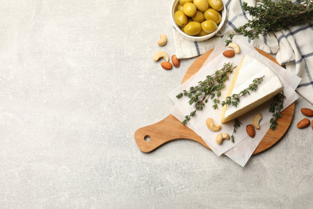 Piece of tasty camembert cheese, thyme, nuts and olives on gray textured table, flat lay. Space for textの写真素材