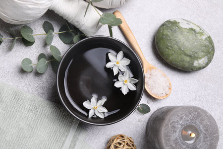 Flat lay composition with herbal massage bags, spa products and flowers on light gray table