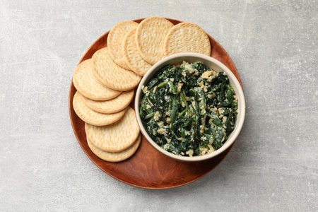 Tasty spinach dip with egg and crackers on gray table, top view