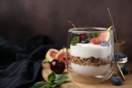 Glass with yogurt, berries, mint and granola on wooden table. Space for textの写真素材