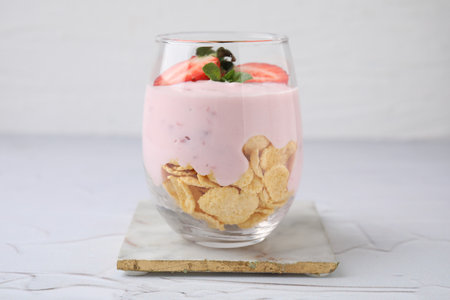 Glass with yogurt, strawberries and corn flakes on white textured tableの写真素材