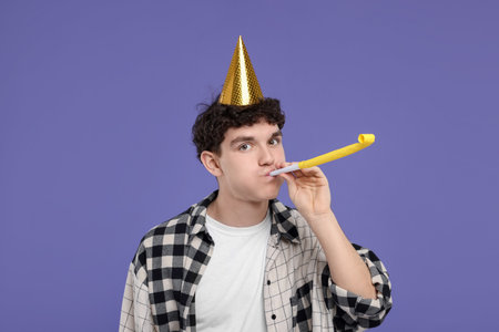 Young man in party hat with blower on purple backgroundの写真素材