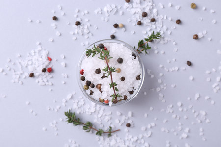 Salt with peppercorns and thyme in bowl on light table, flat layの写真素材