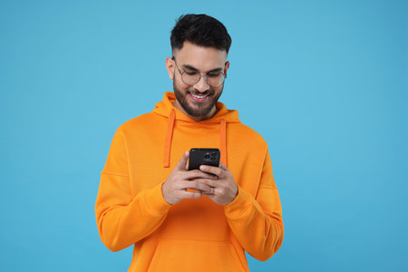 Happy young man using smartphone on light blue background