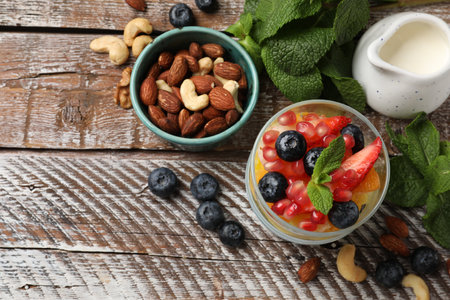 Delicious fruit salad, fresh berries, mint and nuts on wooden table, flat lay. Space for textの写真素材