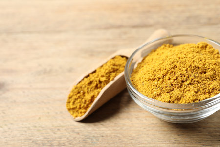Curry powder in bowl and scoop on wooden table, closeup. Space for textの写真素材