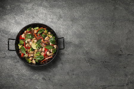 Stir-fry. Tasty noodles with meat and vegetables in wok on gray textured table, top view. Space for textの写真素材