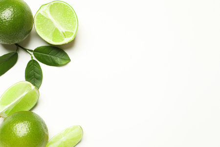Whole and cut fresh ripe limes with green leaves on white background, flat lay
