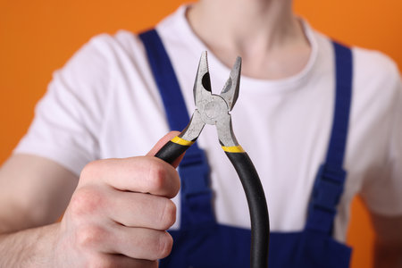 Young man holding pliers on orange background, closeupの写真素材
