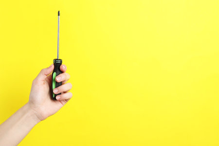 Woman holding screwdriver on yellow background, closeup. Space for textの写真素材