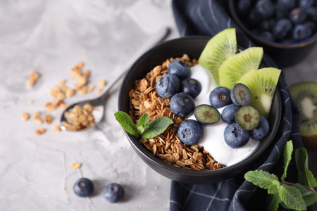 Tasty granola with yogurt, blueberries and kiwi in bowl on gray table, closeupの写真素材